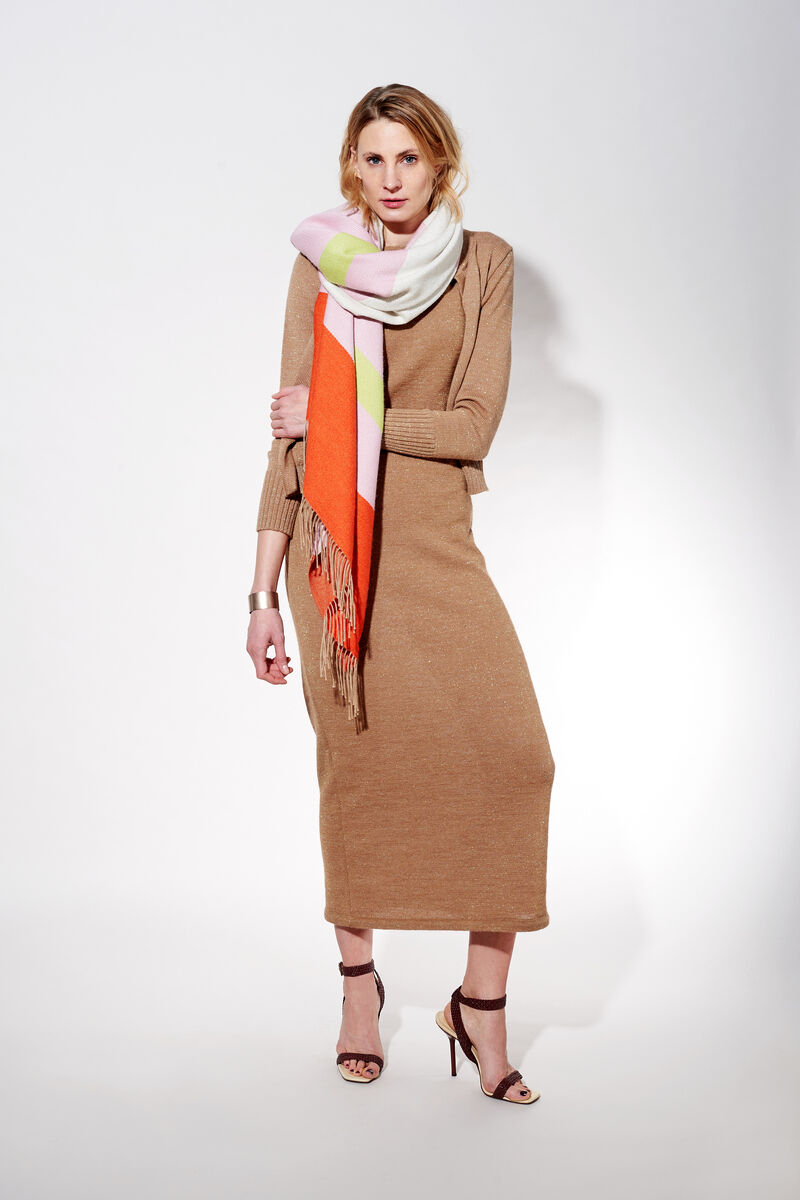 Eine Frau trägt ein langes beigefarbenes Kleid und einen farbenfrohen, gemusterten Schal aus Alpaka-Wolle über den Schultern.