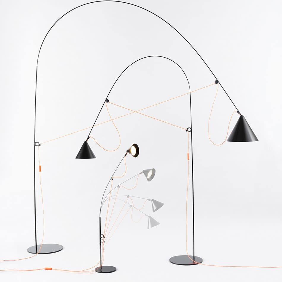 Bild zeigt mehrere Stehlampen »AYNO« mit schlanken, gebogenen Stangen und unterschiedlich ausgerichteten Lampenschirmen in Schwarz, Grau, und Weiß auf weißem Hintergrund. Orange Kabel verlaufen entlang der Stangen.