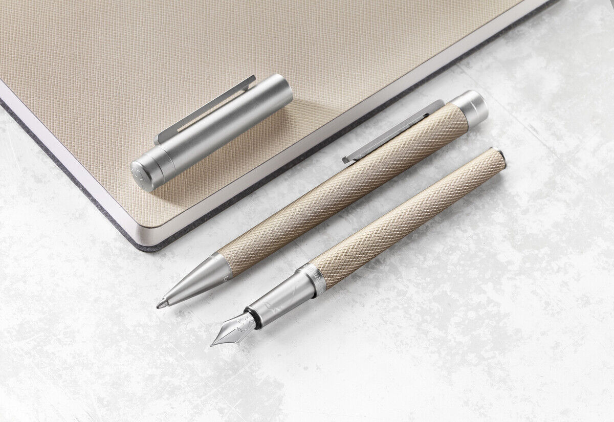 Rollerball Slim Edition - Ein schlafes Design aus Edelstahl wird über ein beiges Notizbuch dargestellt. Es zeigt einen hochwertigen Rollerball-Stift und einen Füllfederhalter, beide in metallischem Silber. Perfekt für Büro und Schule.