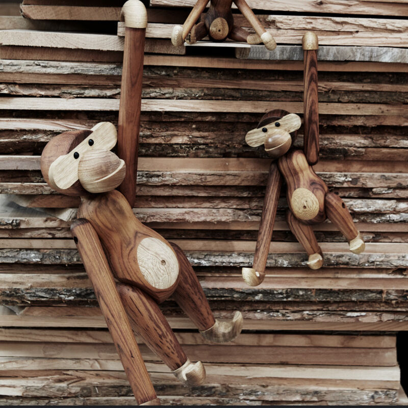 Mehrere detailreich gearbeitete Holzfiguren „Affe“ von Kay Bojesen hängen an Armen auf gestapelten Holzlatten. Die Affen bestehen aus helleren und dunkleren Holzteilen, wirken freundlich und sind im skandinavischen Designstil gefertigt.