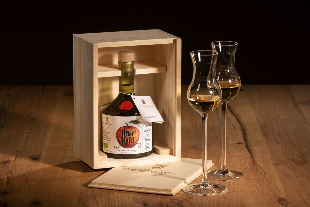 Eine Flasche ZEIT-Sonderedition »Alter Apfel« Edelbrand in einer Holzkiste präsentiert, mit zwei edlen Schnapsgläsern auf einem Holzuntersetzer.