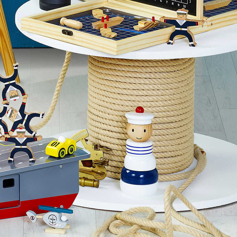 Ein Set von Holzspielzeugen mit maritimem Thema, darunter eine Stapelfigur, die als Matrose verkleidet ist, ein Segelboot und weitere Spielelemente im Hintergrund.