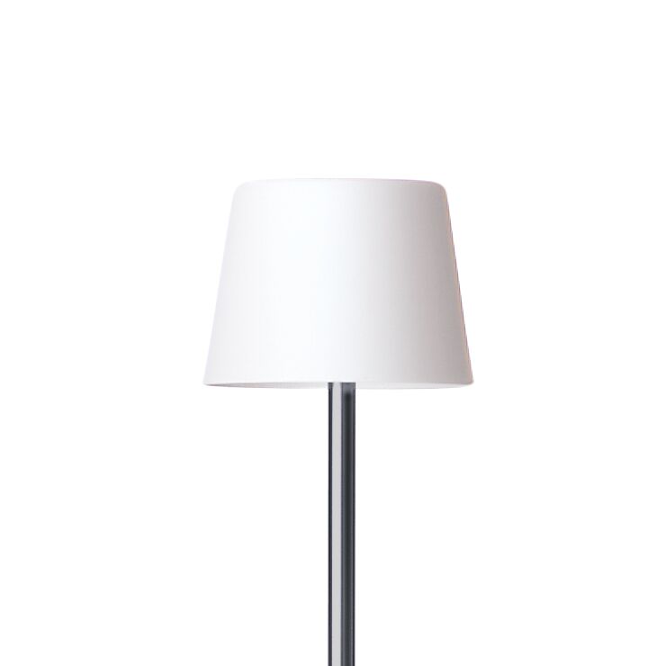 Die Stehlampe »ANTA Cut« der ZEIT Sonderedition steht mittig im Bild. Sie hat einen schlichten zylindrischen, leicht konischen Schirm aus transluzentem weißem Bone China Porzellan und ein schlankes, grau lackiertes Aluminiumstandrohr. Das Design ist minimalistisch und modern.