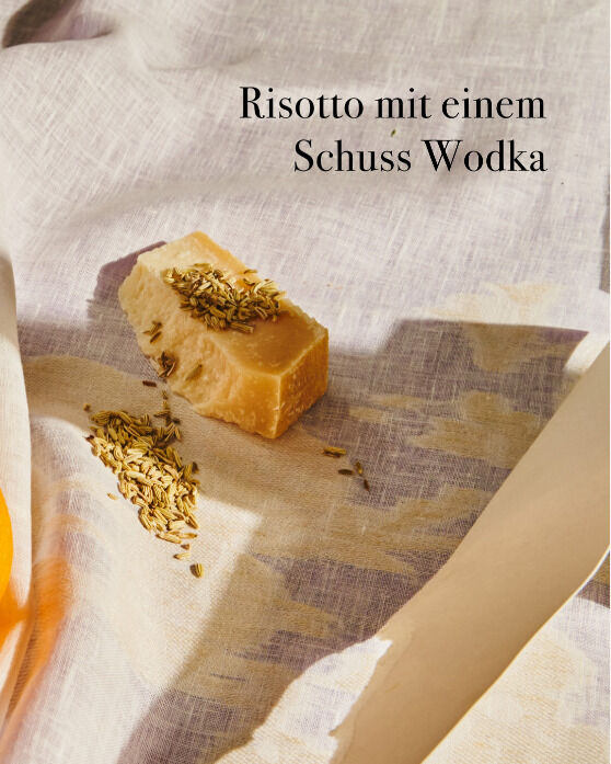 Fotografie eines Kochbuchs mit dem Titel „Wochenmarkt - Vegetarisch“. Der Text auf der Seite lautet 'Risotto mit einem Schuss Wodka'. Abgebildet ist ein Stück Käse mit Körnern und ein Tuch im Hintergrund.