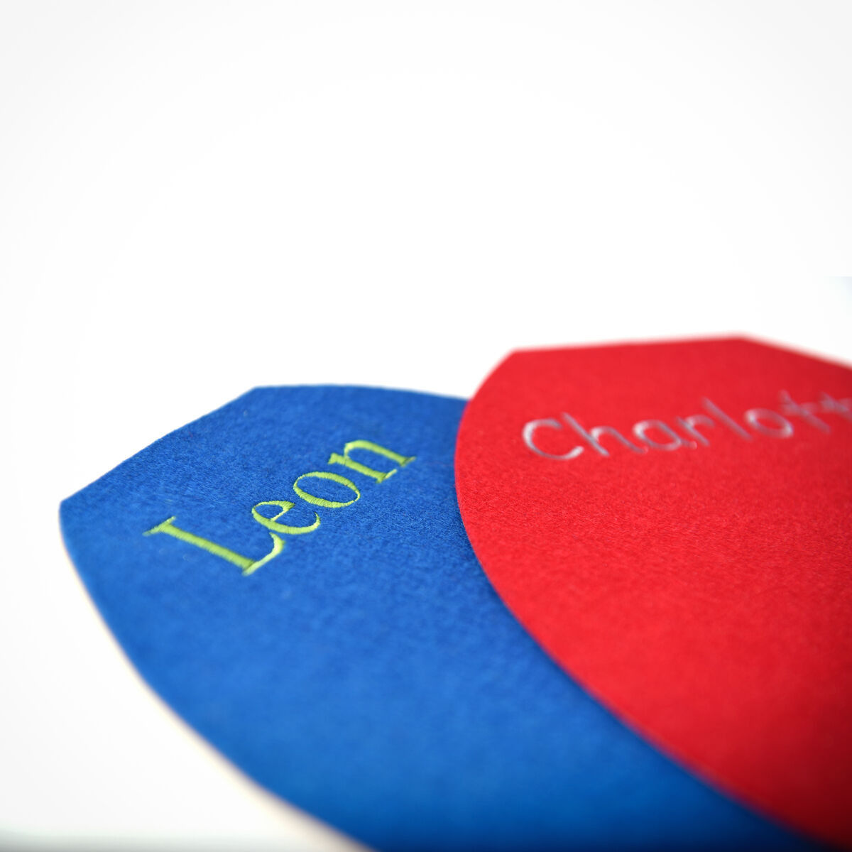 Zwei Papphocker in den Farben Blau und Rot, personalisiert mit den Namen Leon und Charlotte in Gelb und Weiß, auf weißem Hintergrund.
