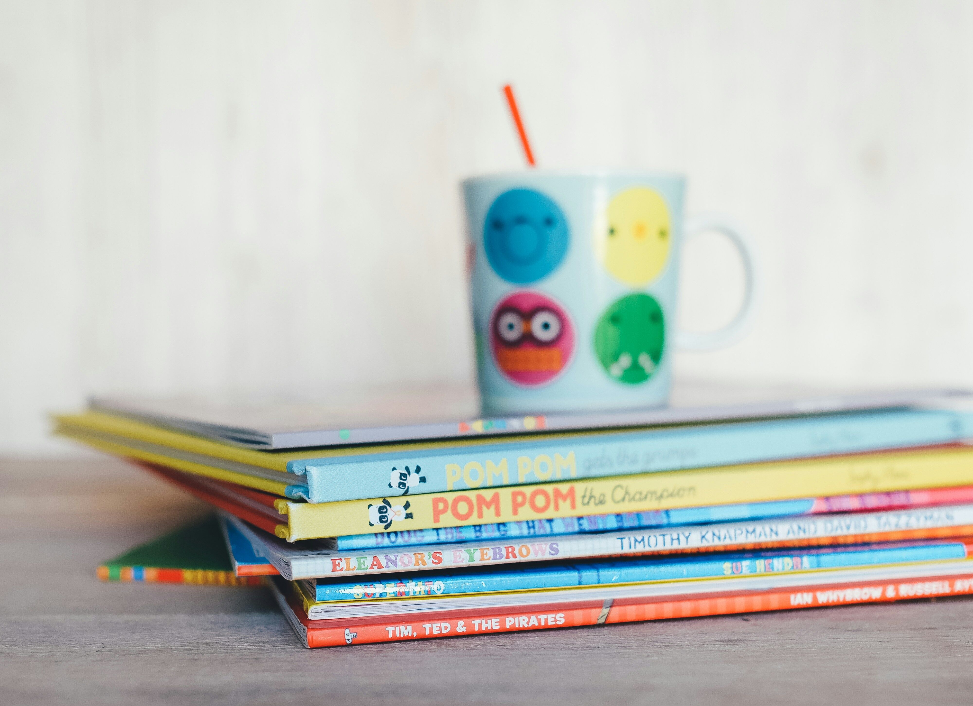 alt="Gestapelte Kinderbücher und ein Kinderbecher, die die Kategorie Kinderbücher darstellen soll "
