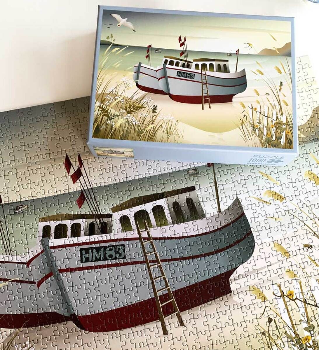 Ein Puzzle mit einem Motiv von Fischerbooten am Strand, farbenfroh in Blau, Weiß und Rot, mit einem natürlichen Hintergrund aus Meer und Dünen.