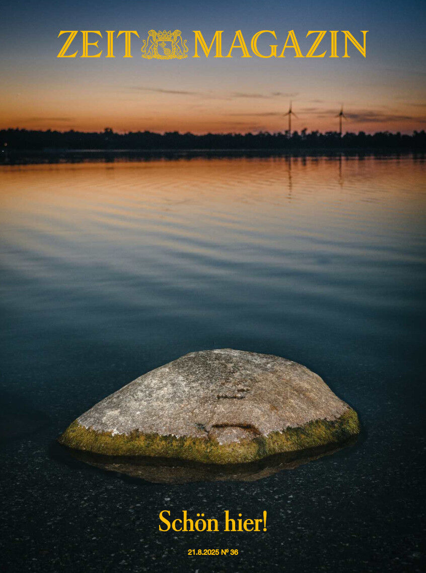 Titelbild des ZEIT Magazins Ausgabe 36/2025 mit einem großen Stein im ruhigen Wasser an einem See bei Sonnenuntergang. Am Horizont sind Windräder und Bäume zu erkennen. Über dem Bild steht der Schriftzug ZEIT MAGAZIN, darunter der gelbe Text 'Schön hier!'