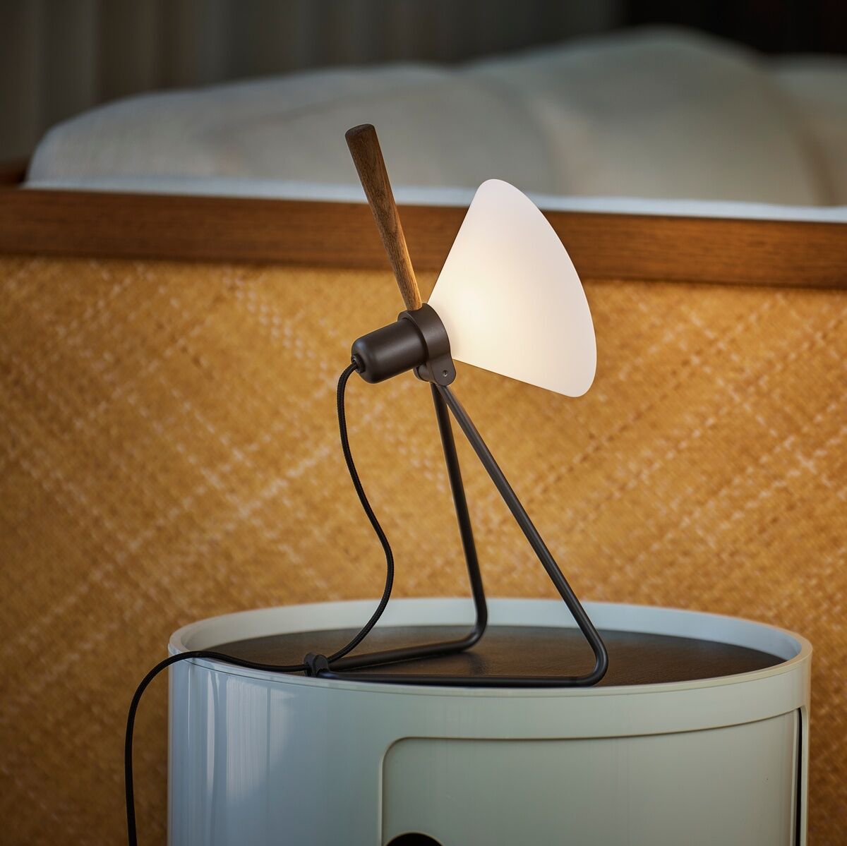 Eine moderne Tisch- oder Hängelampe namens 'Spot', bestehend aus einem weißen Lampenschirm in minimalistischem Design. Die Lampe steht auf einem runden, zweifarbigen Beistelltisch vor einer holzgerahmten, strukturierten Rückwand.