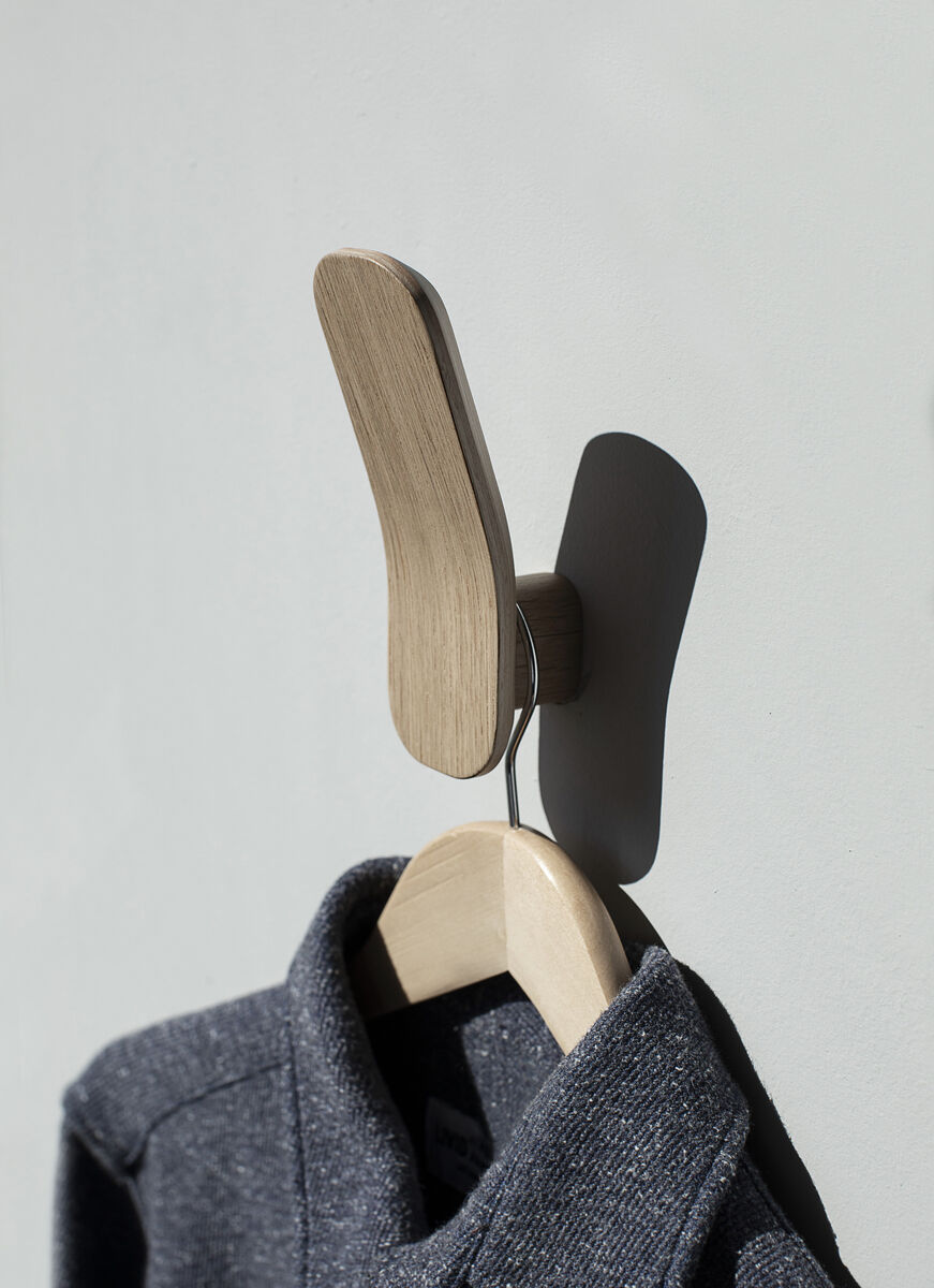 Ein moderner Kleiderhaken aus Eiche-Holz mit einem minimalistischen Design. An der Wand befestigt, hängt ein graues Kleidungsstück an einem Holzbügel.