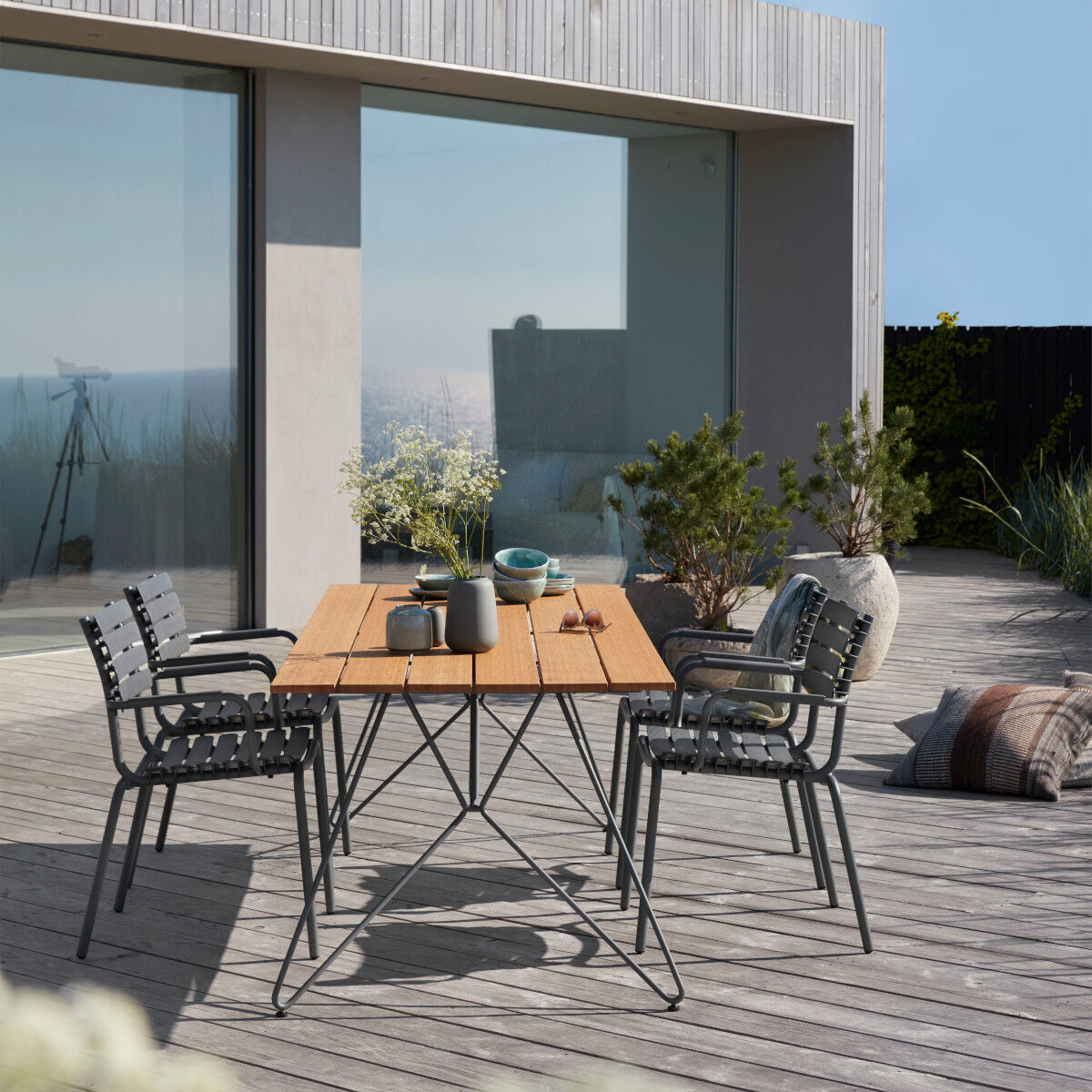 Moderner Gartentisch »Sketch« aus Holz auf einer Terrasse mit Stühlen, Pflanzen und Dekorationen für den Außenbereich.