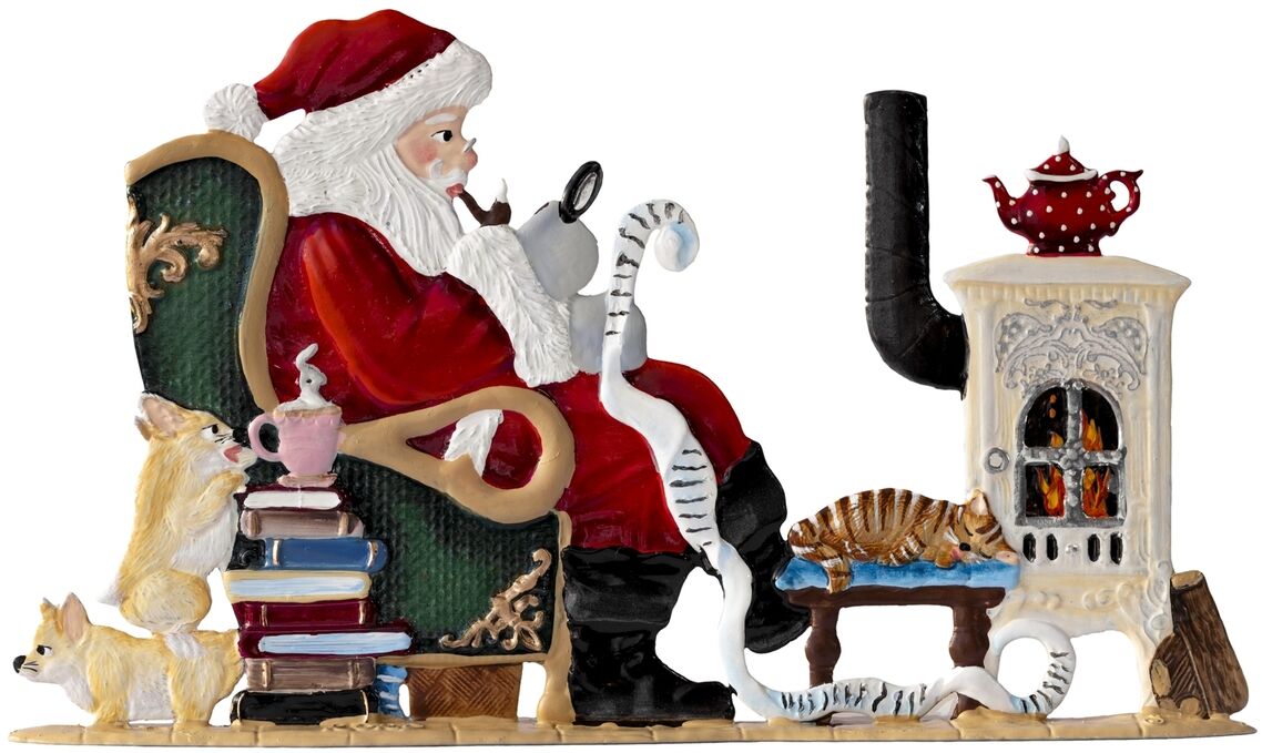 Zinnfigur zeigt Weihnachtsmann auf grünem Sessel, der in eine Wunschliste schaut, flankiert von Hund, Katze, Bücherstapel, rosafarbener Tasse, brennendem Ofen mit roter Teekanne und gemütlicher Wohnzimmerszene. Geeignet als festliche Dekoration zu Weihnachten.