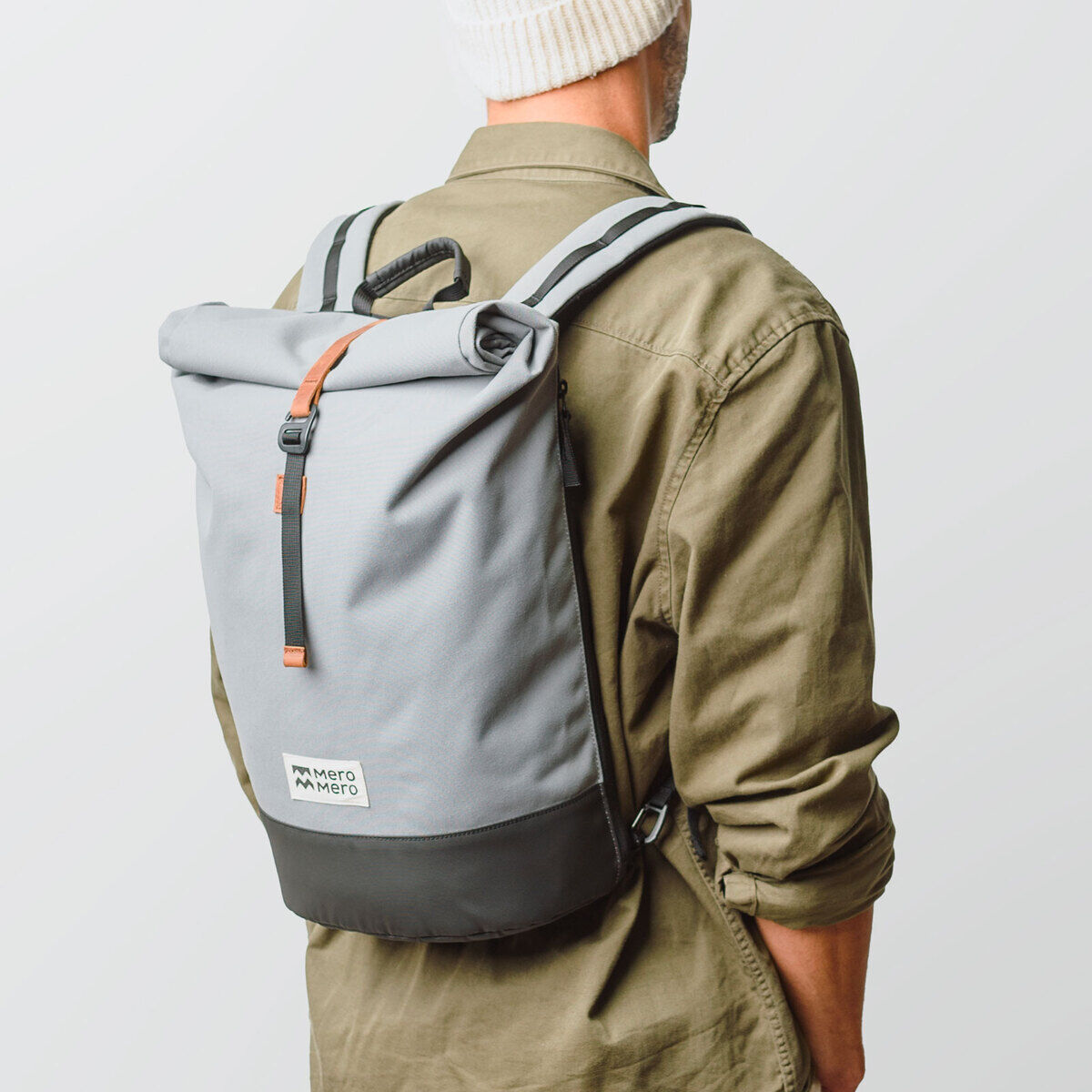 Person trägt einen grauen Fahrradtasche/Rucksack »Annecy« auf dem Rücken. Der Rucksack hat einen schwarzen Bodensteil und braune Akzentdetails. Die Person trägt ein grünes Hemd und eine graue Beanie-Mütze.