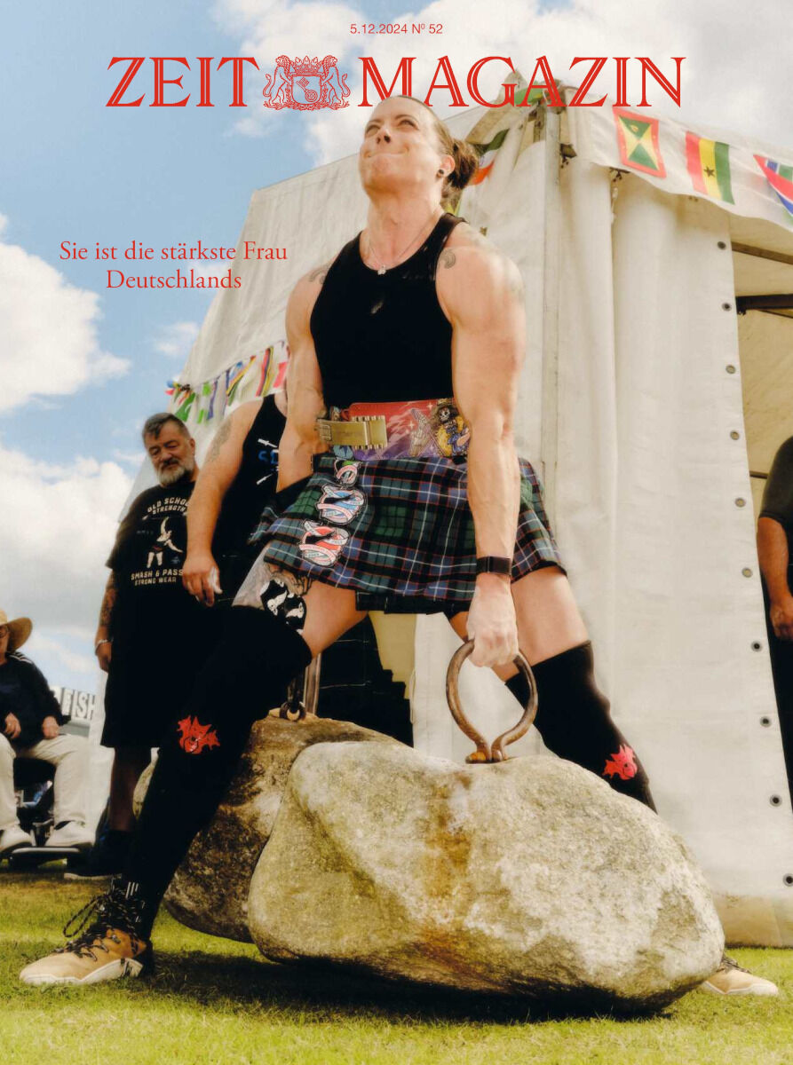 Auf dem Titelbild des ZEIT Magazins 52/2024 ist eine Frau beim Steinheben während der Highland Games zu sehen. Sie trägt einen traditionellen Kilt. Im Hintergrund sind ein Zelt und eine Fahne erkennbar.