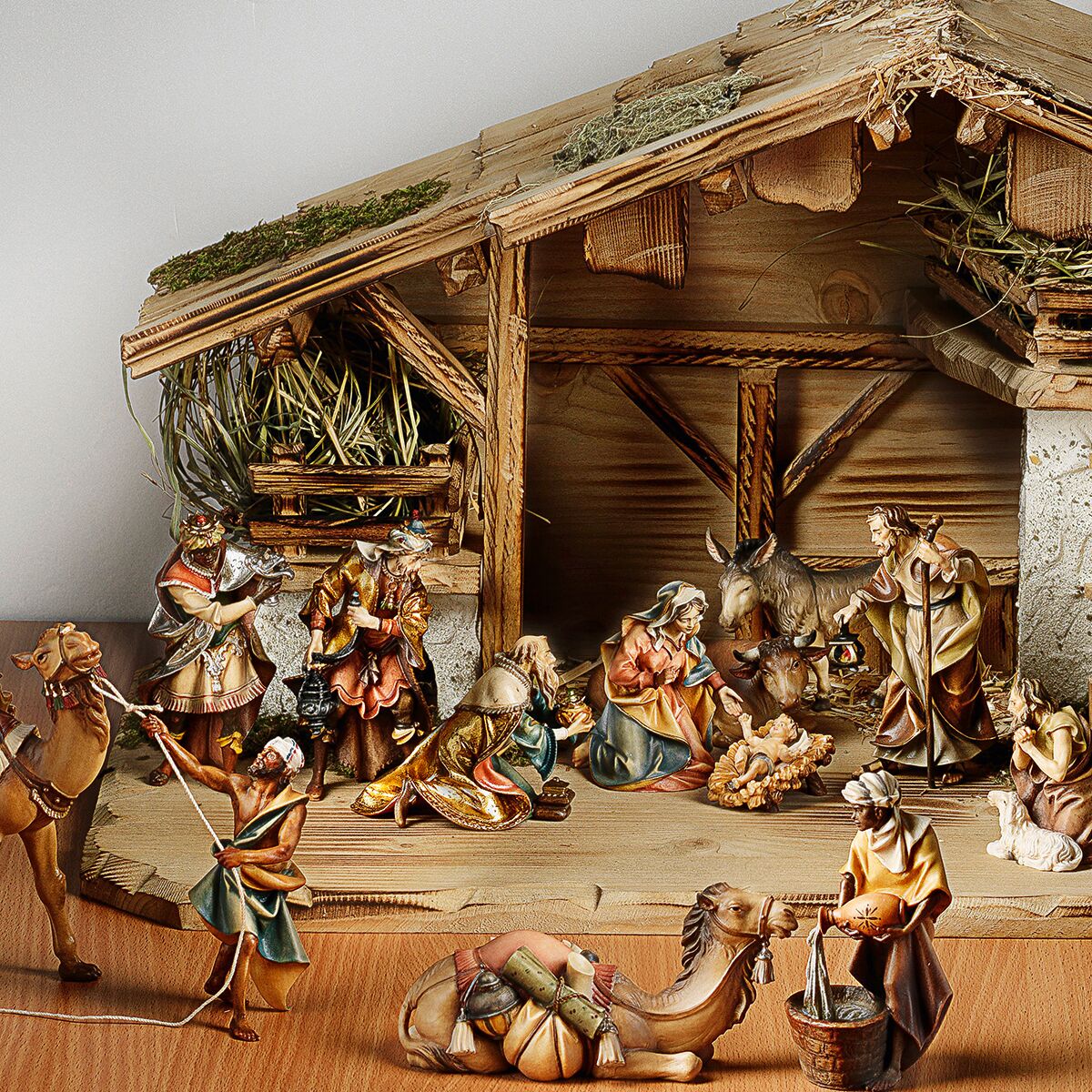 Handgeschnitzte 20-teilige Holzkrippe zeigt eine detaillierte Weihnachtskrippenszene mit Heilige Familie, Tieren, Hirten und den Heiligen Drei Königen in einem offenen Stall mit Stroh und rustikalem Dach. Die Figuren sind liebevoll gestaltet und in warmen Naturfarben bemalt.