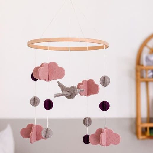 Ein Mobile aus Filz mit rosa und grauen Wolken und Punkten, das an einem runden Holzrahmen hängt. Ideal zur Dekoration von Baby- und Kinderzimmern.