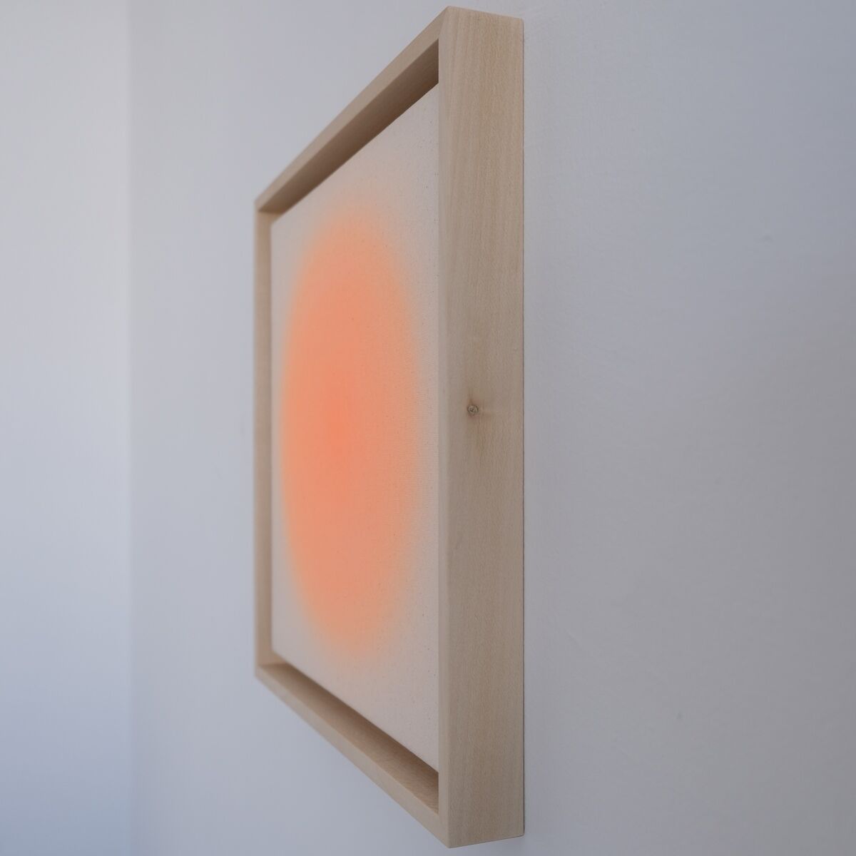 Das Bild zeigt ein gerahmtes, modernes Kunstwerk mit einem weichen, orangefarbenen Farbverlauf in der Mitte auf weißem Grund. Der Holzrahmen ist schlicht gehalten und das Bild hängt an einer weißen Wand. Die Farben verlaufen sanft und erzeugen eine beruhigende, minimalistische Atmosphäre.