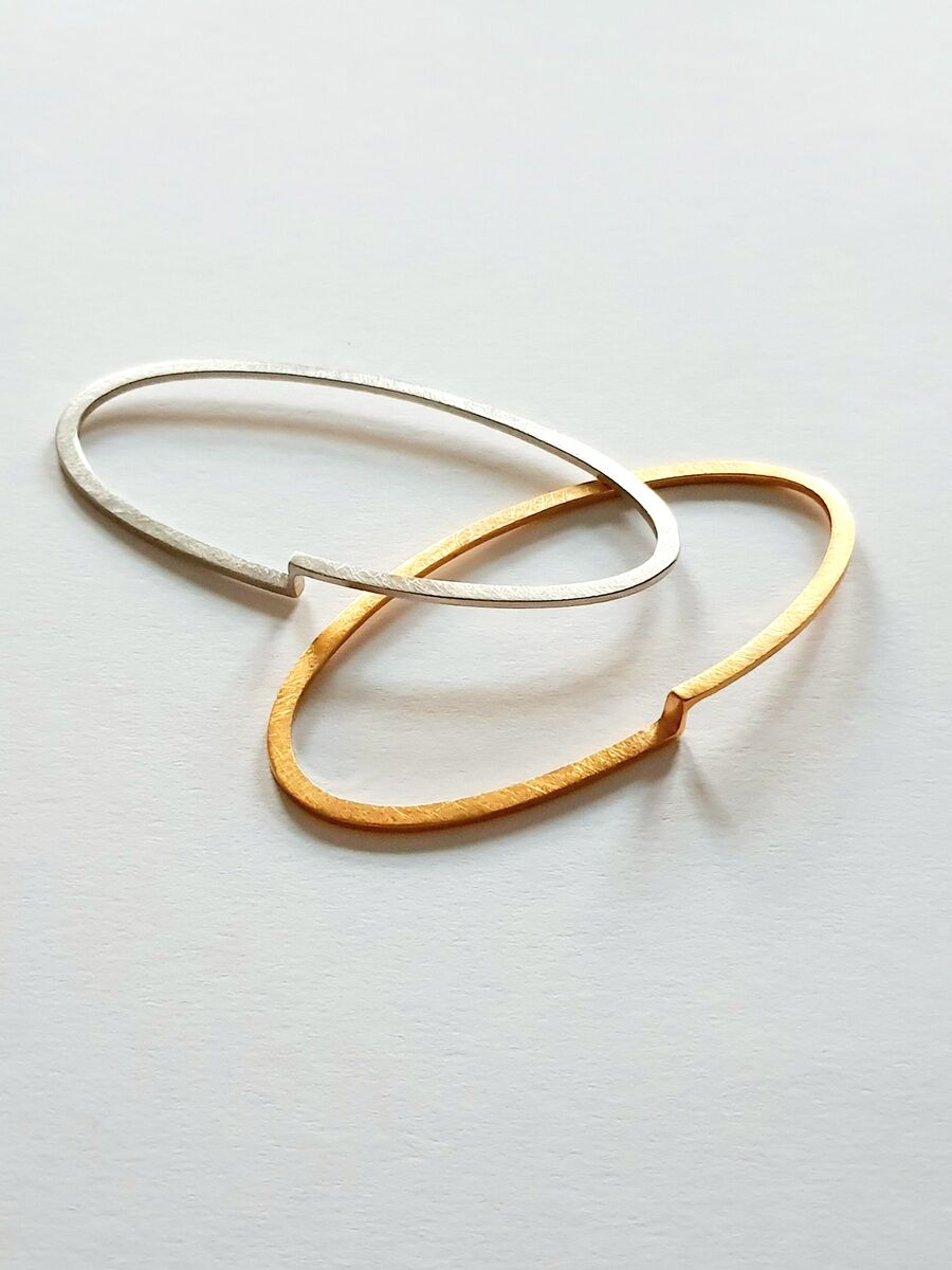 Zwei schlichte, elegante Armreife in Gold und Silber auf weißem Hintergrund.