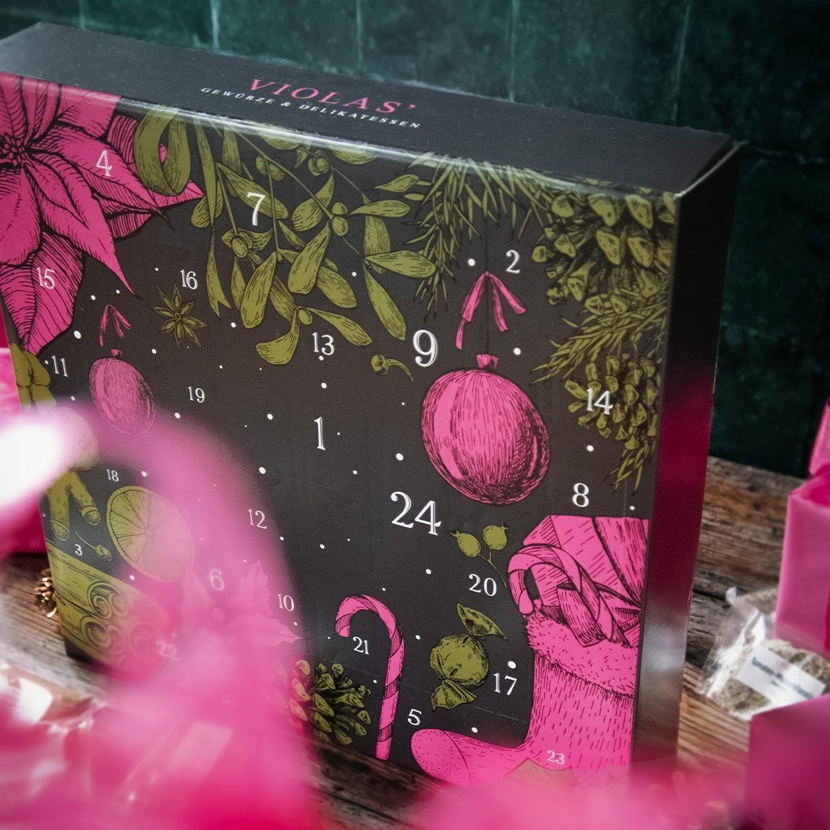 Ein schwarzer Adventskalender von Violas mit pinken und grünen Elementen, einschließlich Sternen, Zahlen und Festtagsdekorationen.