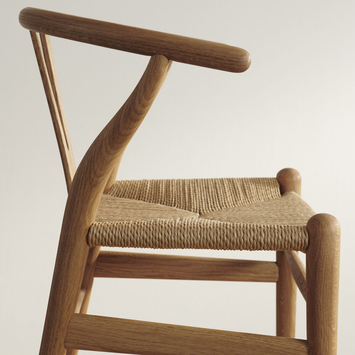 Seitlicher Blick auf einen Wishbone Chair »CH24 Kinder« aus Holz mit geflochtenem Sitz, vor einem hellen Hintergrund.