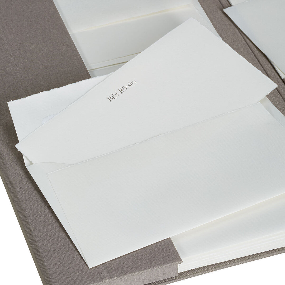 Eine Briefpapiermappe mit edlem Büttenpapier. Zu sehen sind mehrere Blätter helles Papier und Briefumschläge in einer braunen Mappe angeordnet.
