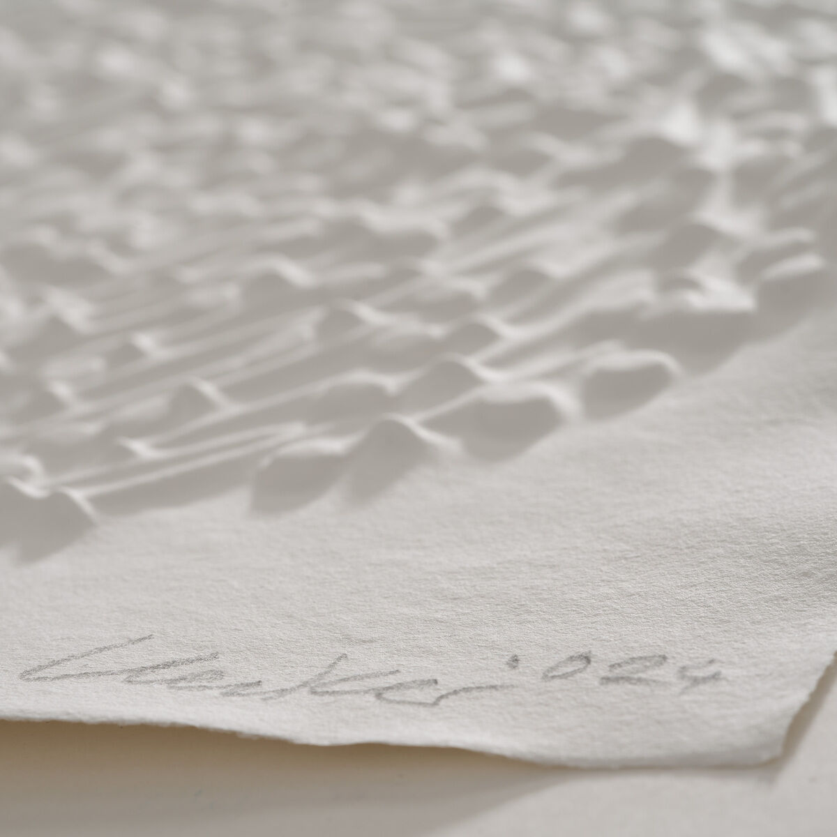 Ein Prägedruck von Günther Uecker mit einer wellenartigen Struktur auf hellem Papier. Das Kunstwerk ist unten rechts mit 'Uecker 2021' signiert.