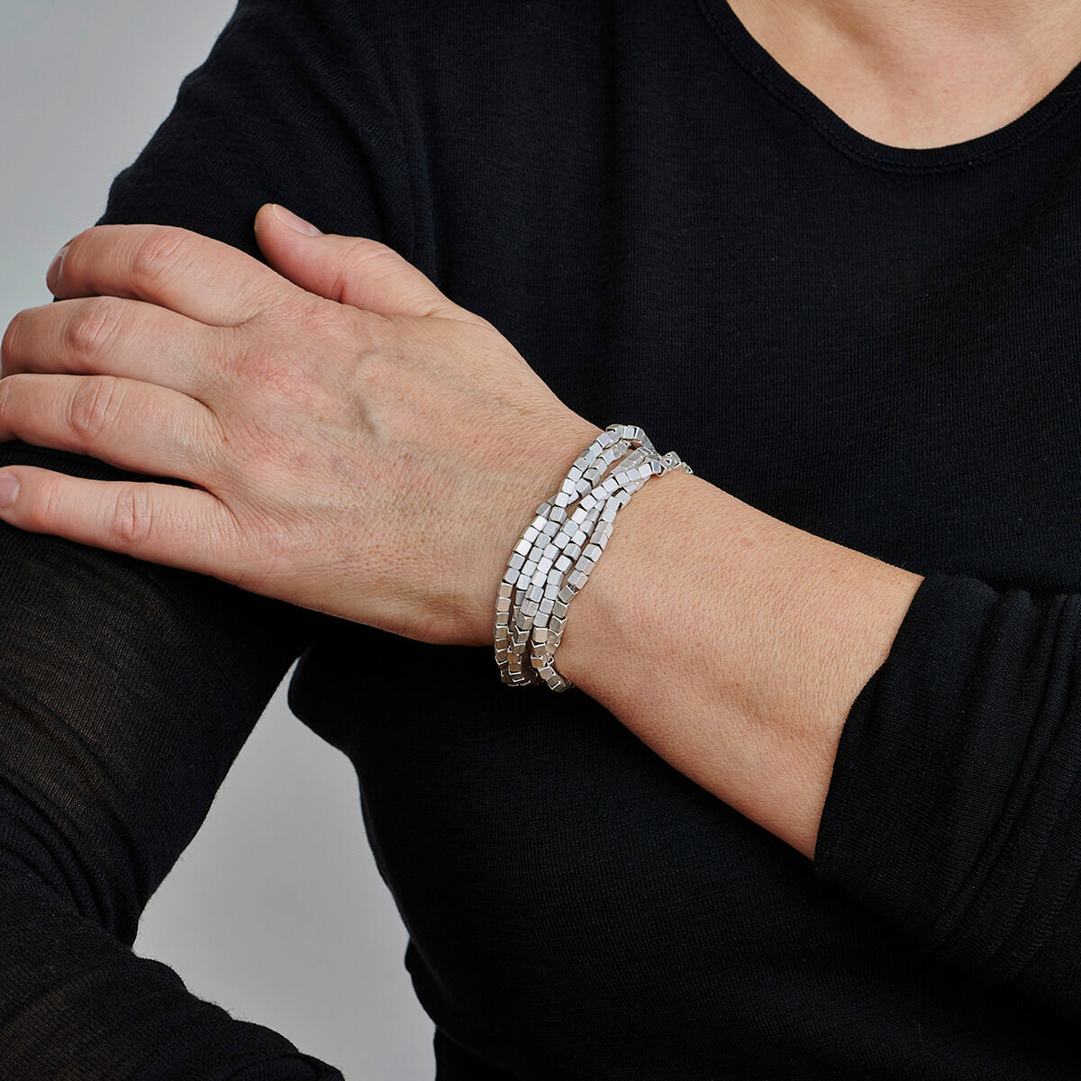 Nahaufnahme einer silbernen Kette mit Würfelanhänger, getragen über einer schwarzen Bluse. Die Kette ist elegant und hat ein minimalistisches Design, passend für verschiedene Anlässe.