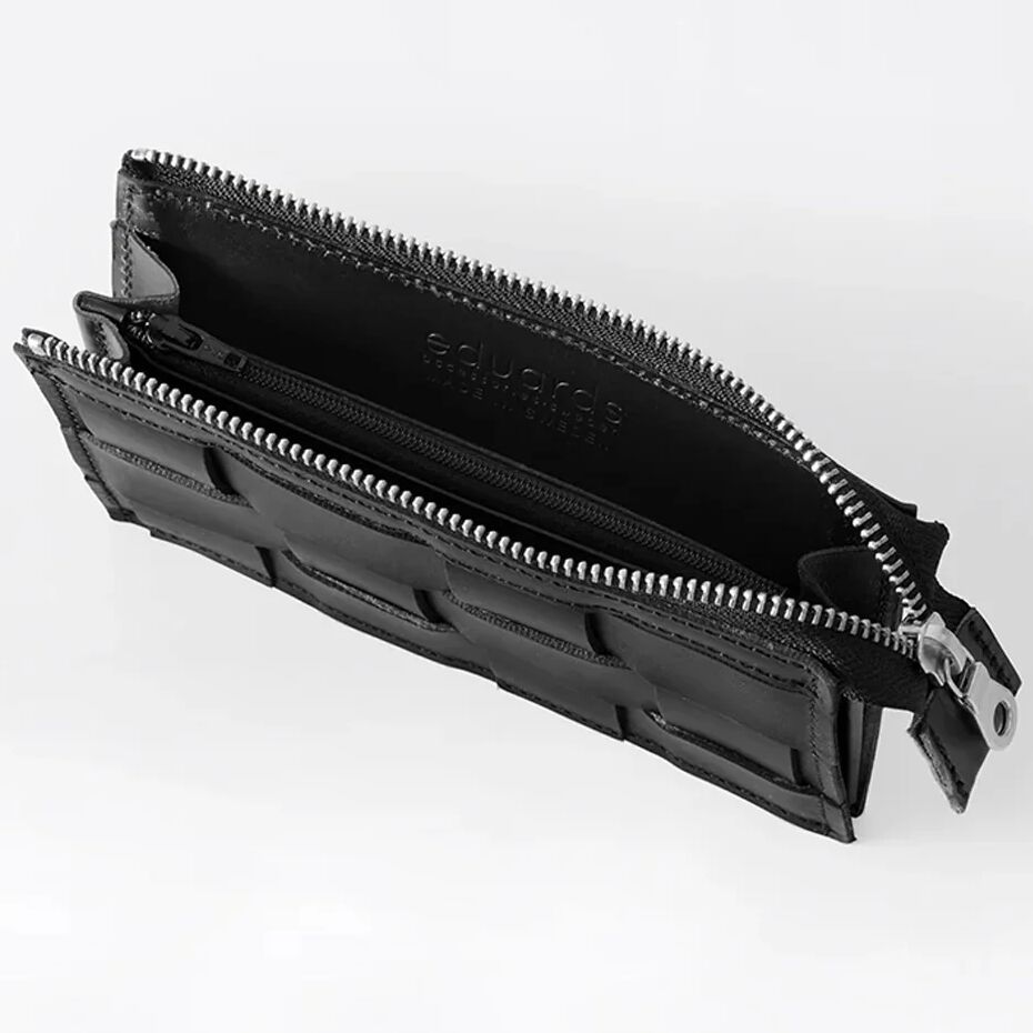 Schwarze, handgefertigte Brieftasche »Näver« von Eduards Accessories AB, aus pflanzlich gegerbtem Leder mit geflochtener Vorderseite. Sichtbar sind zwei offene Fächer und ein mittiges Reißverschluss-Innenfach. Der Reißverschluss ist silberfarben. Maße: ca. 16,5 x 11 cm.