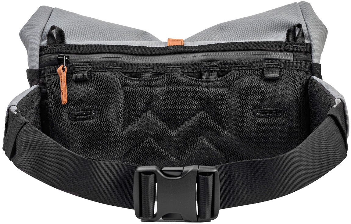 Eine Tasche namens »Piha« in überwiegend schwarzer und grauer Farbe mit einem verstellbaren schwarzen Gurt und einem Reißverschluss oben. Die Tasche hat braune Akzente an den Reißverschlüssen und ist aus strapazierfähigem Material gefertigt.