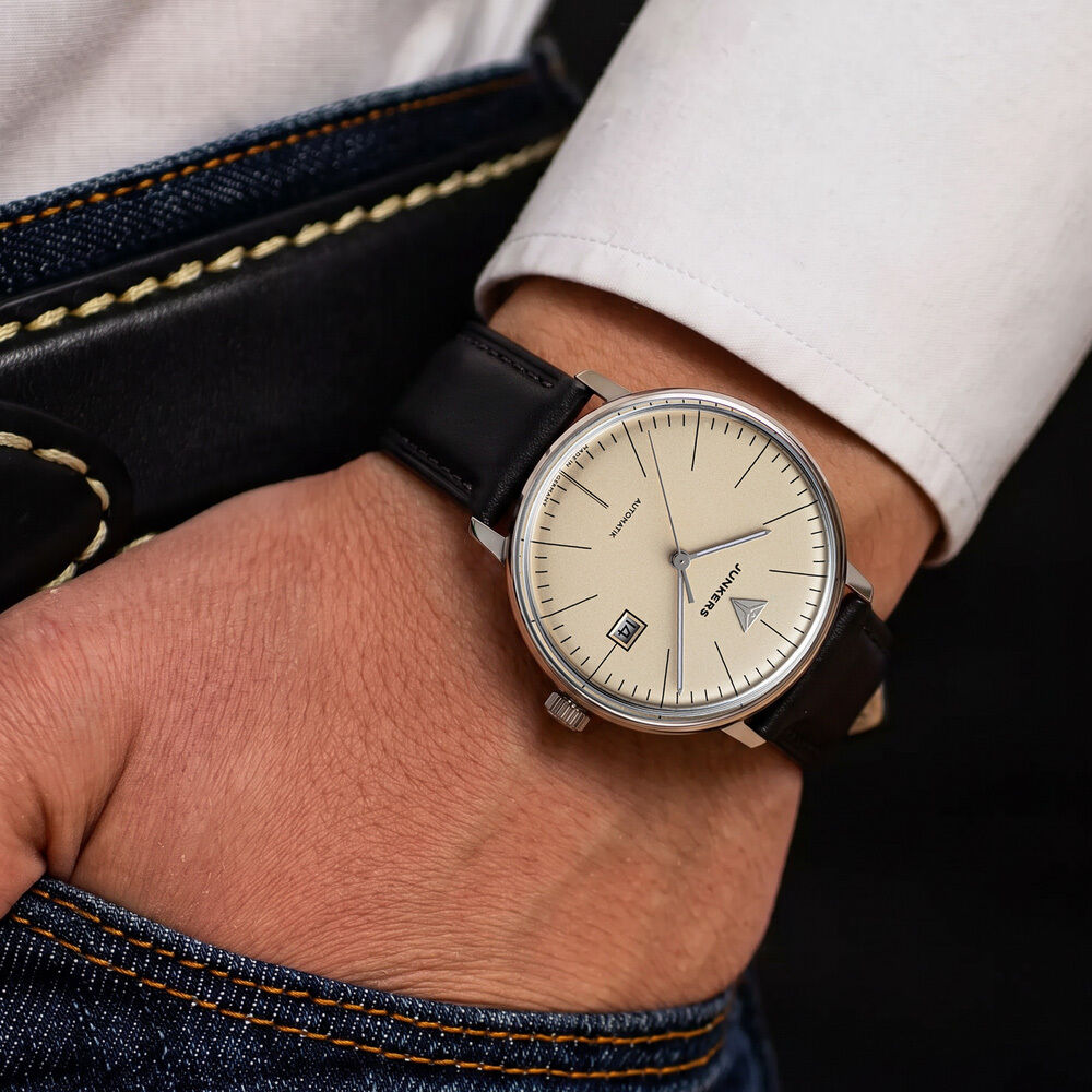 Nahaufnahme eines Handgelenks mit der ZEIT-Sonderedition Uhr »Bauhaus Automatik« von Junkers. Die Uhr hat ein beiges Zifferblatt, klare Indizes, ein Datumsfenster, silbernes Edelstahlgehäuse und ein schwarzes Lederarmband. Modern, minimalistisch, elegant.