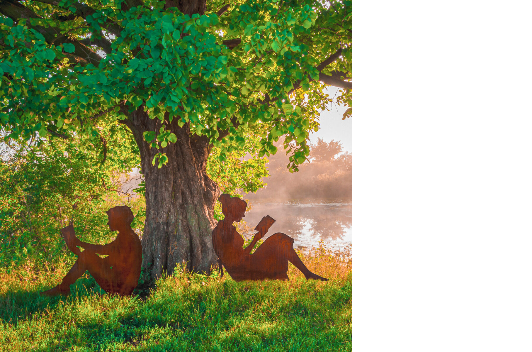 Gartenfigur Silhouette 'Lesende und Lesender' Paar zeigt zwei Silhouetten aus Metall, die unter einem Baum sitzen und lesen, mit einem See im Hintergrund und Sonnenstrahlen durch das Laub.