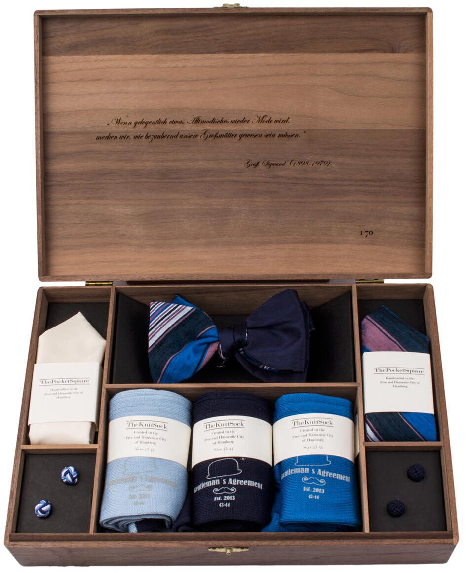 ZEIT-Accessoire-Set #46 in einer eleganten Holzbox. Enthalten sind vier Krawatten, zwei Einstecktücher und zwei Paar Manschettenknöpfe. Die Krawatten sind in verschiedenen Blautönen und Mustern gestaltet. Ein Geschenkset für stilbewusste Herren, geeignet für formelle Anlässe.
