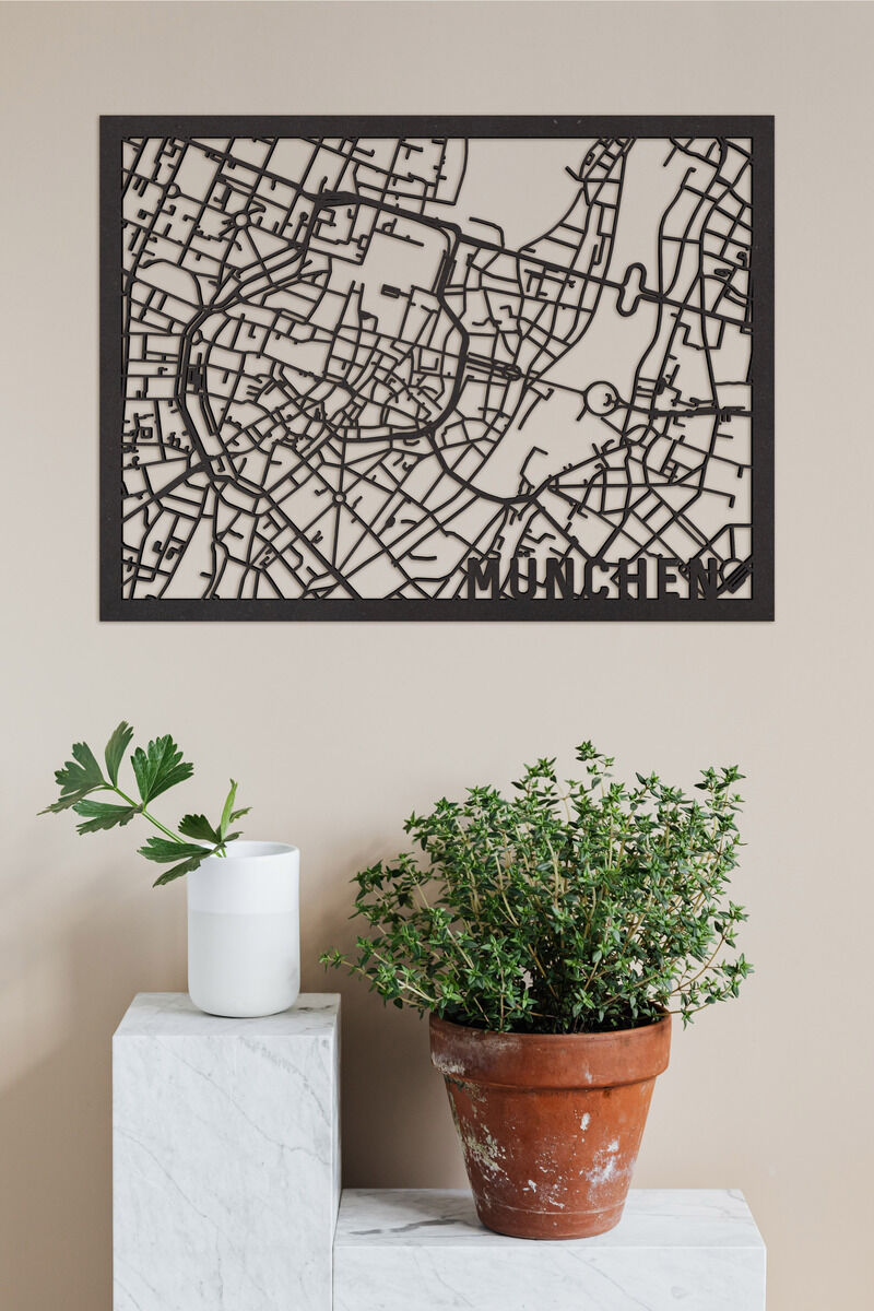 Citymap »München« aus Holz mit detailliertem Stadtplan. Wanddekoration hängt an beiger Wand, daneben eine Pflanze in einem Terrakottatopf und eine weiße Kerze auf einem weißen Podest.