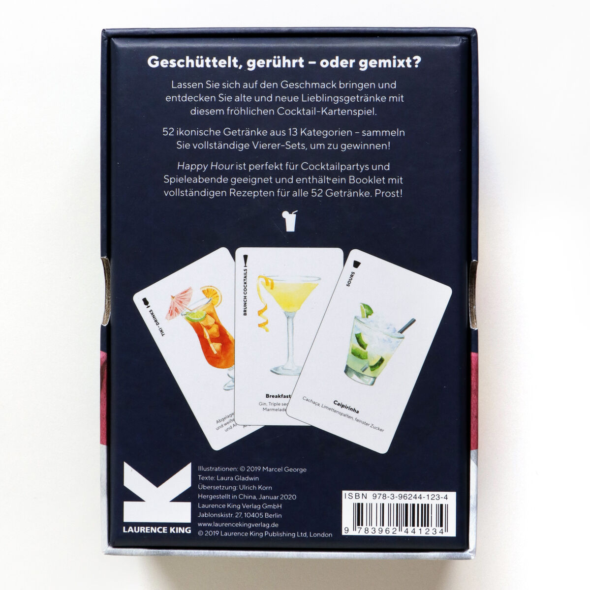 Packung des Gesellschaftsspiels 'Happy Hour - Ein Cocktailspiel' zeigt drei Cocktailkarten mit verschiedenen Cocktailbildern und Rezepten, darunter ein roter, ein gelber und ein weißer Cocktail. Text auf der Verpackung beschreibt das Spielkonzept und es sind Barcode und Verlagslogo sichtbar.