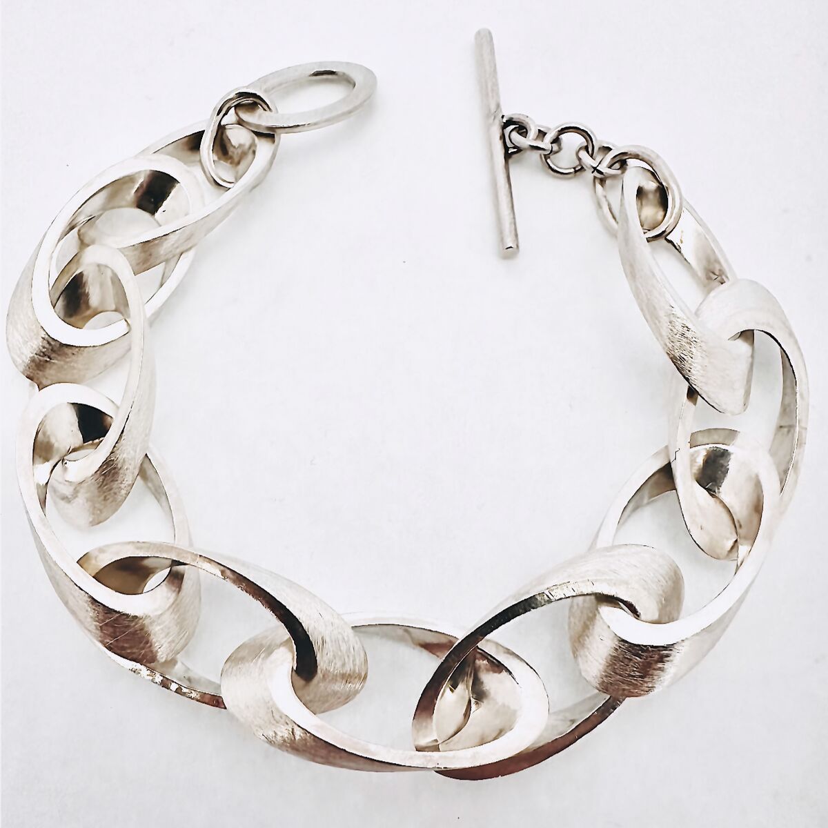 Silbernes Kettenarmband mit großen, flachgedrückten Gliedern und einem T-Verschluss, auf weißem Hintergrund dargestellt.