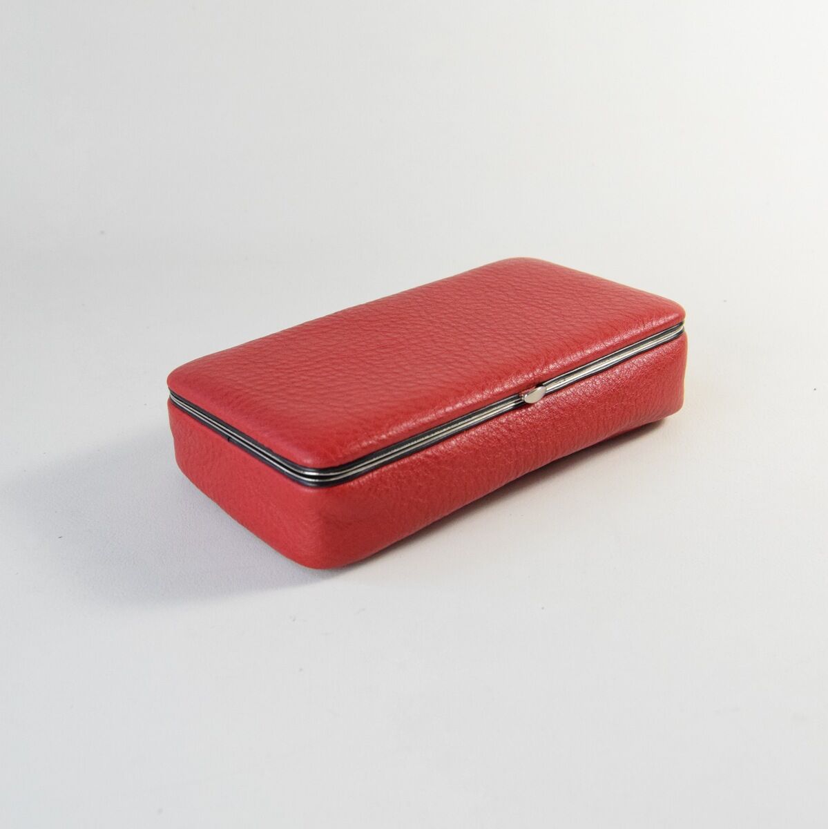 Eine rote Utensilienbox aus Leder mit einem schlichten und eleganten Design. Sie hat eine rechteckige Form mit abgerundeten Kanten und einem metallischen Rand.