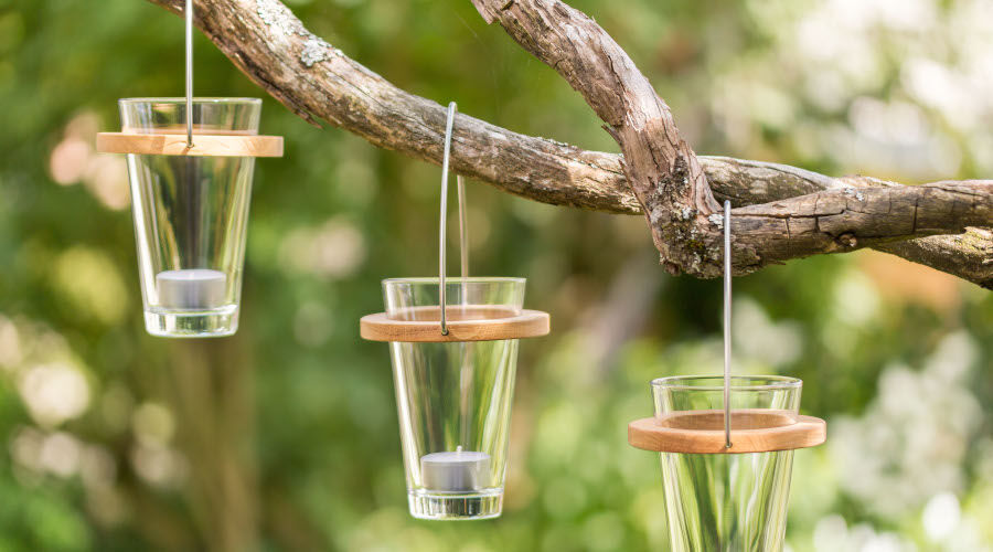 Drei hängende Windlichter aus Glas mit Holzringen an einem Ast im Garten