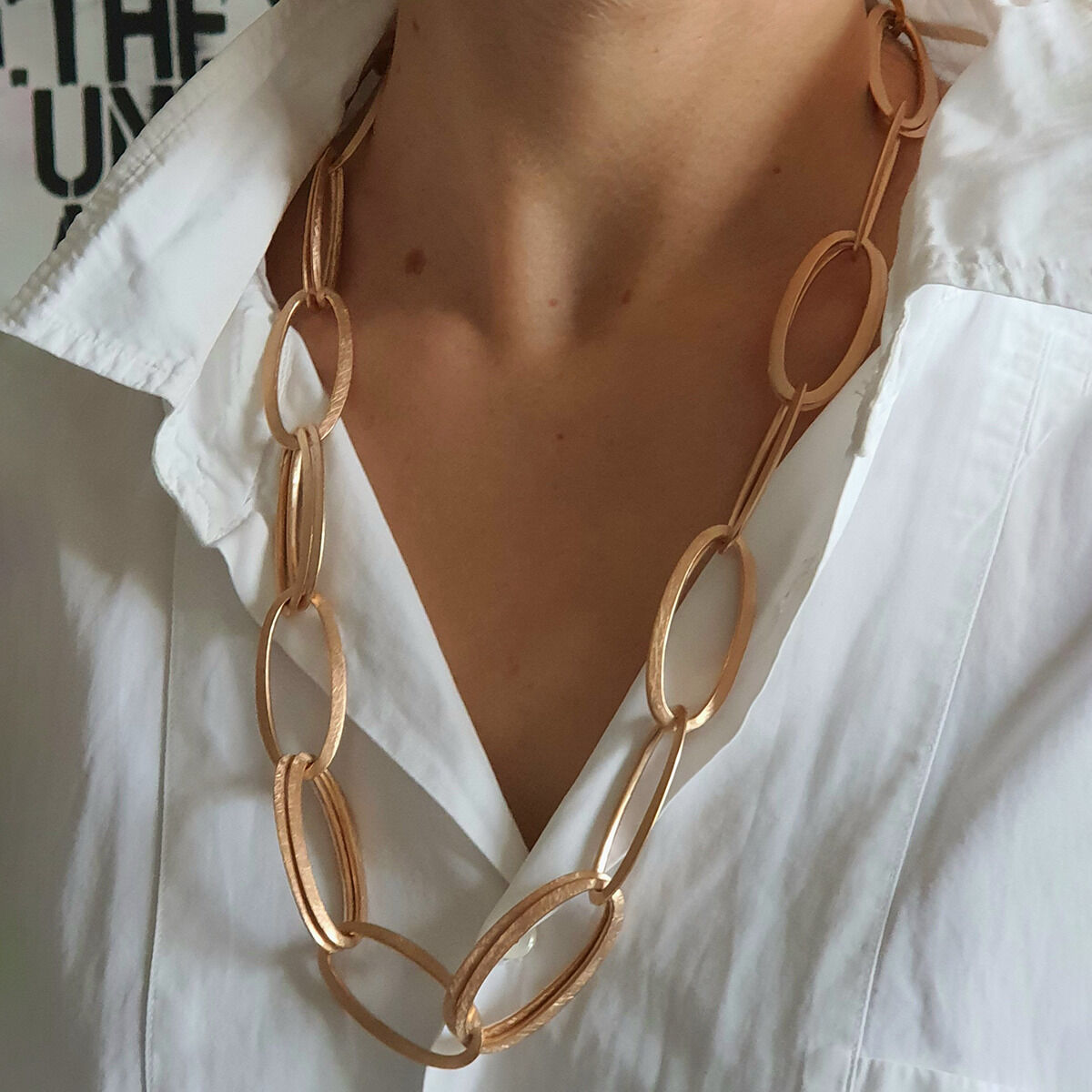 Eine Frau trägt das Collier »GRACE« von HML Berlin in Roségoldplattierung zu einer weißen Bluse. Die Halskette besteht aus großen, ovalen, miteinander verbundenen Gliedern mit matter Oberfläche und wirkt zeitlos elegant und puristisch.