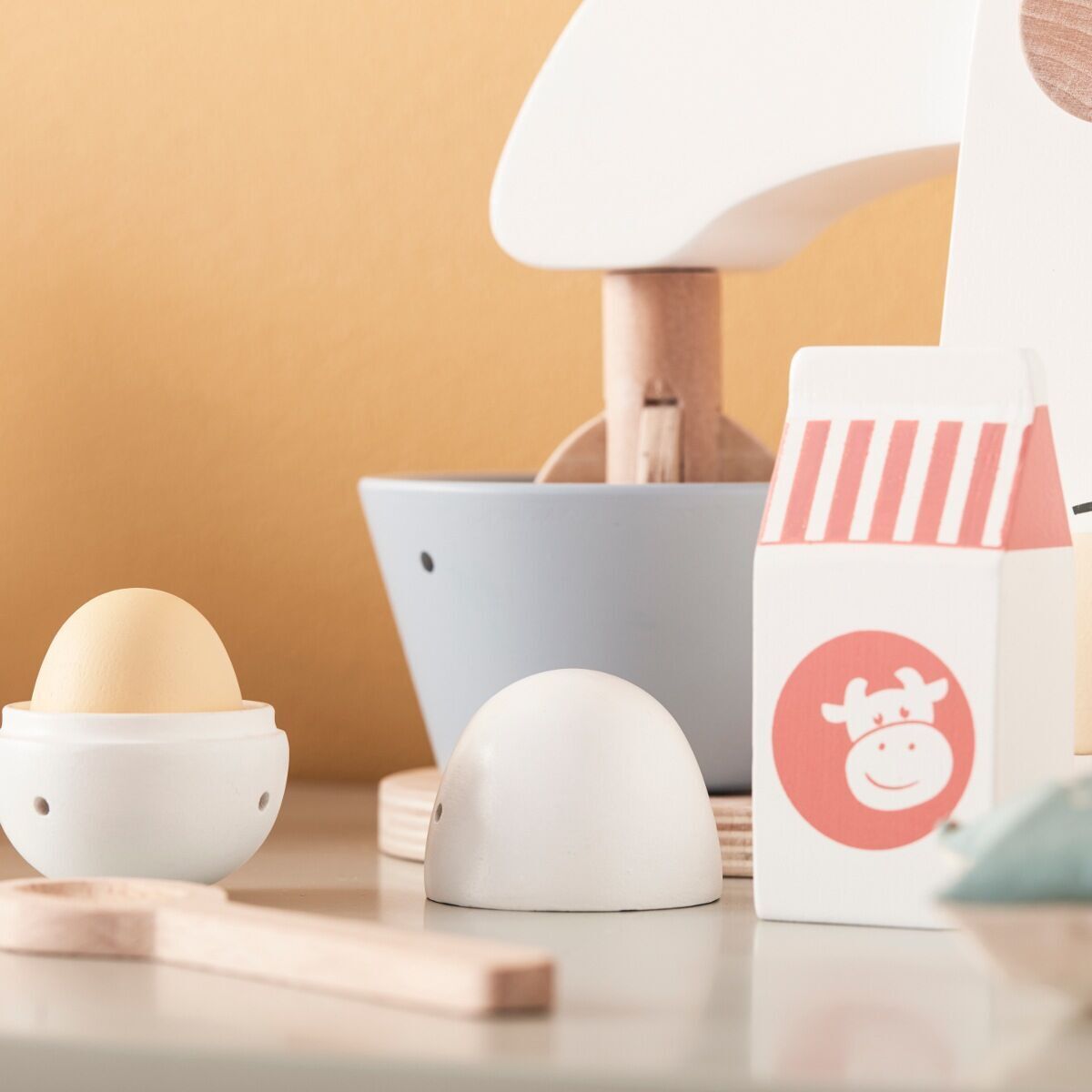 Ein Mixer-Set aus Holz mit Zubehör auf einem Tisch. Das Set enthält einen Holzspielzeug-Mixer, eine Milchpackung, einen Eierbecher und weitere kleine Utensilien. Perfekt für Kinderküchen und spielerisches Lernen.