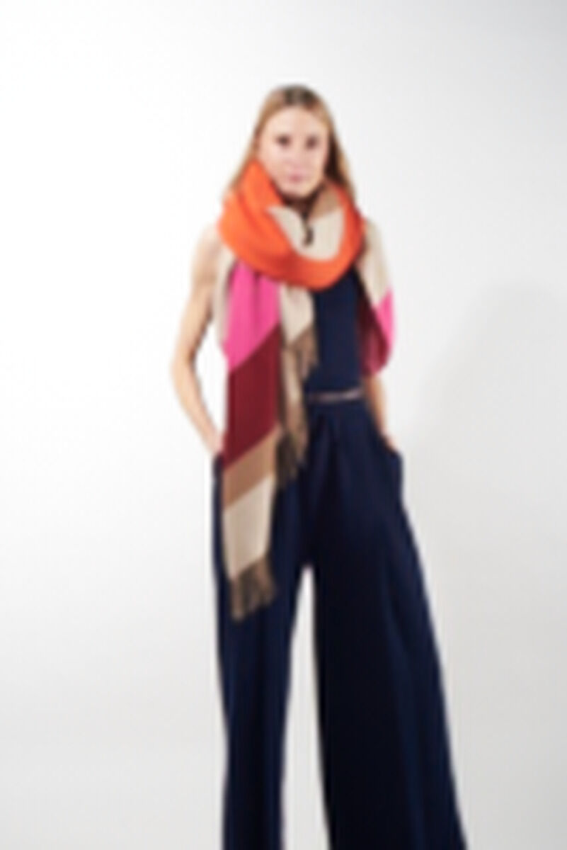 Eine Frau trägt ein buntes Cape aus Alpakawolle in den Farben Orange, Rot, Rosa, Beige und Braun.