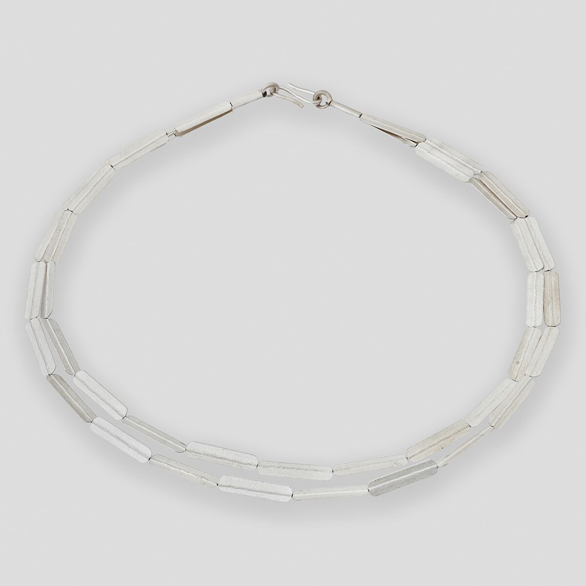 Silbernes Collier mit geprägten, länglichen Stabelementen, die abwechselnd angeordnet sind. Die Halskette wirkt modern und minimalistisch, besonders geeignet als eleganter Halsschmuck für verschiedene festliche Anlässe oder als stilvolles Accessoire im Alltag.