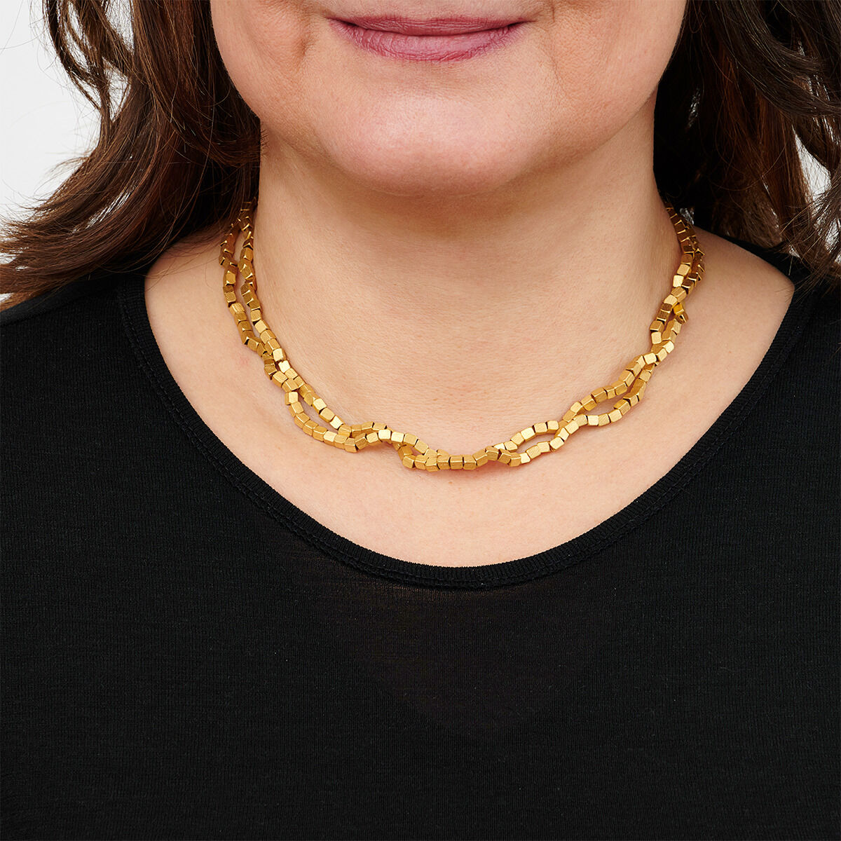 Frau trägt eine goldplattierte Halskette mit würfelförmigen Gliedern über einem schwarzen Oberteil.