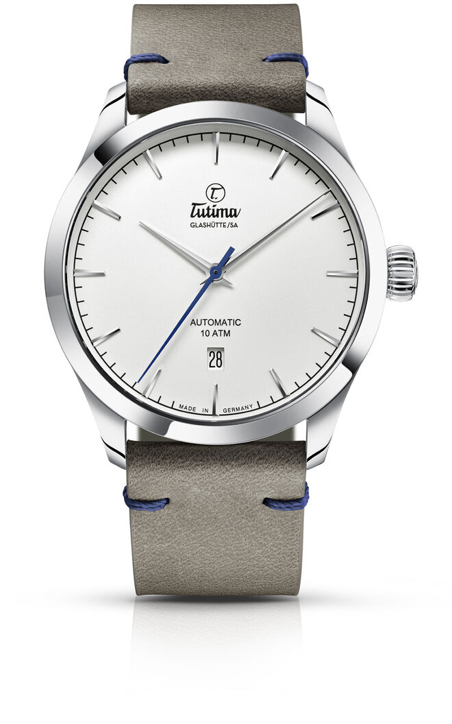 Dieses Bild zeigt die ZEIT Sonderedition »Flieger Aero Club« Automatikuhr von Tutima. Die Uhr hat ein Edelstahlgehäuse und ein graues Lederarmband mit blauen Nähten. Das Zifferblatt ist weiß mit silberfarbenen Markierungen und Zeigern.