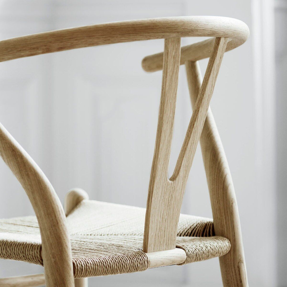 Nahaufnahme eines Wishbone Chair CH24 von Carl Hansen & Søn. Der Stuhl besteht aus naturfarbenem Holz mit einer Y-förmigen Rückenlehne und einem Sitz aus geflochtenem Korb. Das Design ist minimalistisch und zeitlos.