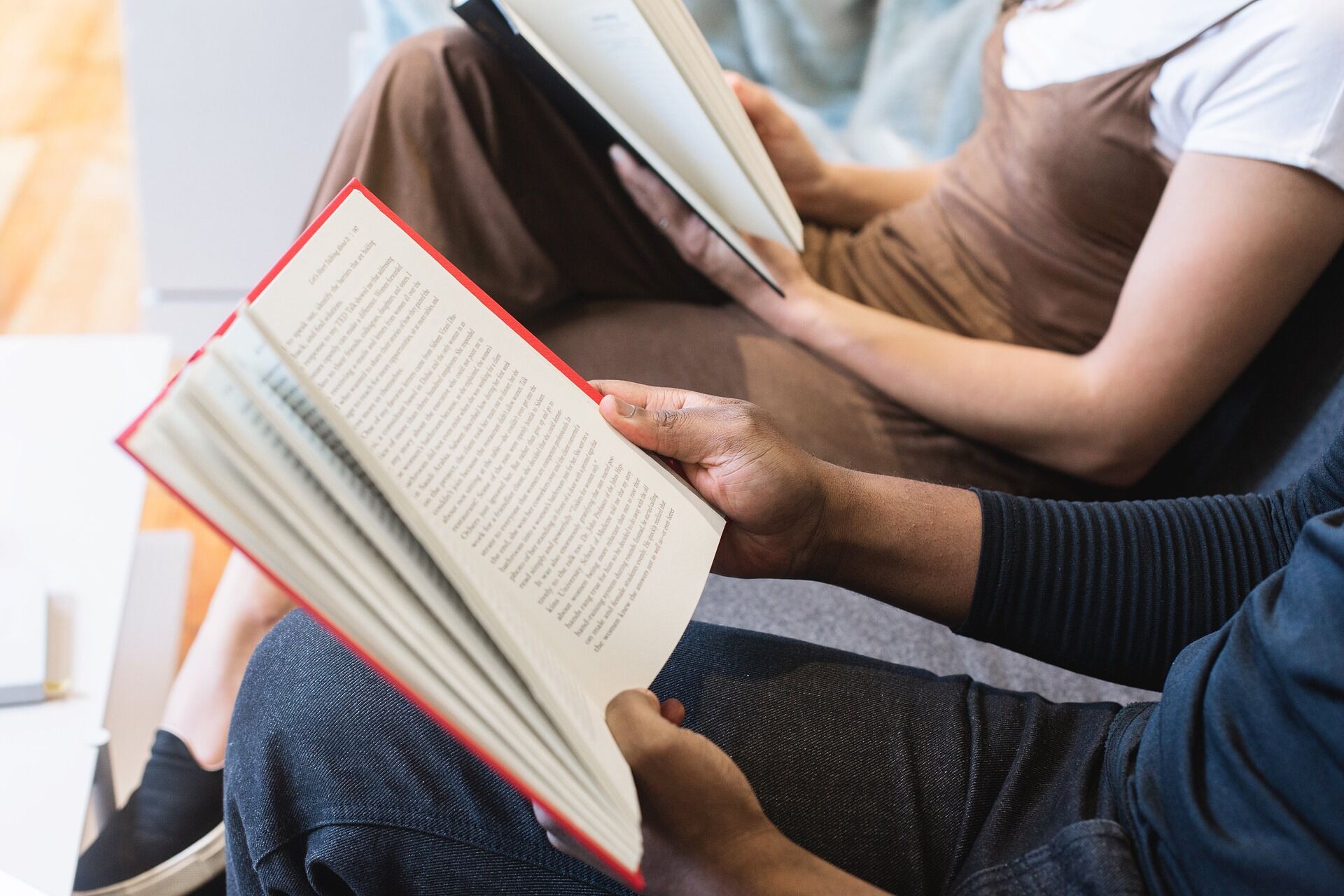 Zwei Personen sitzen nebeneinander und lesen jeweils ein Buch, Nahaufnahme der Buchseiten und der Hände.