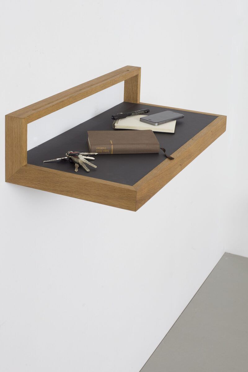Ein wandmontiertes Ablagebord namens »buck« in Anthrazit mit einem Holzrahmen, darauf liegen Schlüssel und Notizbücher. Hintergrund ist eine weiße Wand.