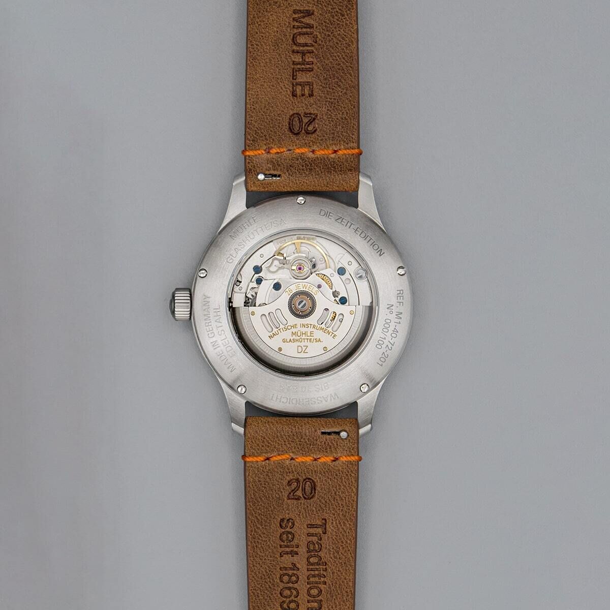 Rückseite einer eleganten Armbanduhr der ZEIT-Sonderedition »Panova Grau« von Mühle Glashütte mit sichtbarem mechanischem Uhrwerk und braunem Lederarmband.
