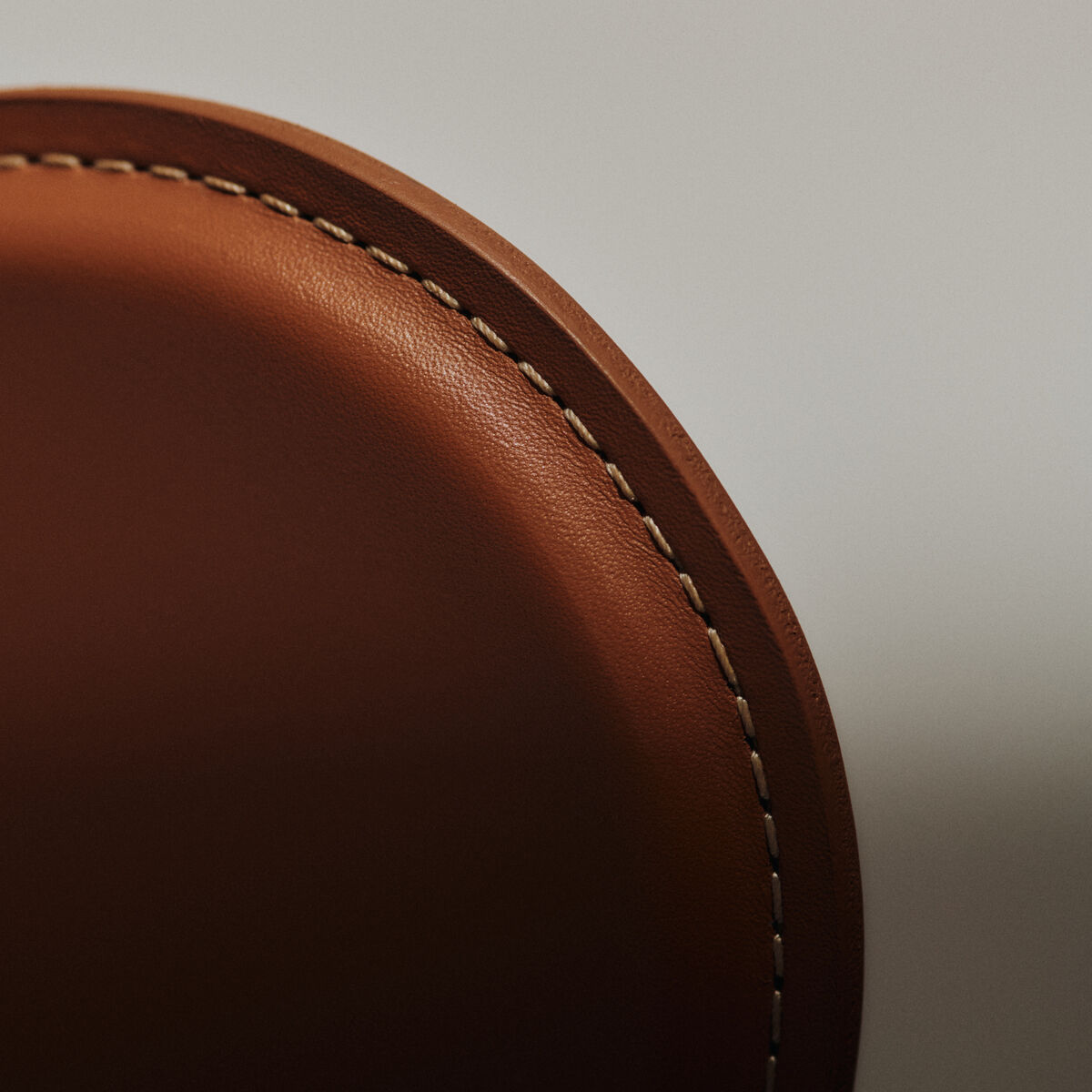 Detailaufnahme einer elegant genähten Rückenlehne des Stuhls »Series 7™ Tailored« von Fritz Hansen. Hochwertiges, sattelbraunes Leder mit markanter, beiger Kontrastnaht. Die sanft gerundete Form hebt die exzellente Verarbeitung und das zeitlose Design hervor.