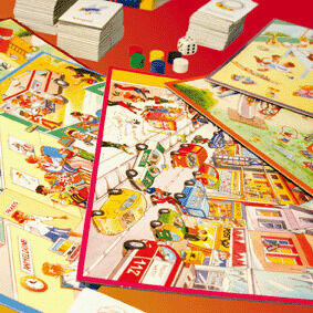 Mehrere bunte Spielbretter des Brettspiels »Sprechdachs« liegen auf einem Tisch verteilt. Darauf zu sehen sind fröhliche, kindgerechte Illustrationen mit alltäglichen Szenen, Würfeln, Spielkarten und farbigen Spielfiguren. Im Hintergrund befinden sich weitere Kartenstapel.
