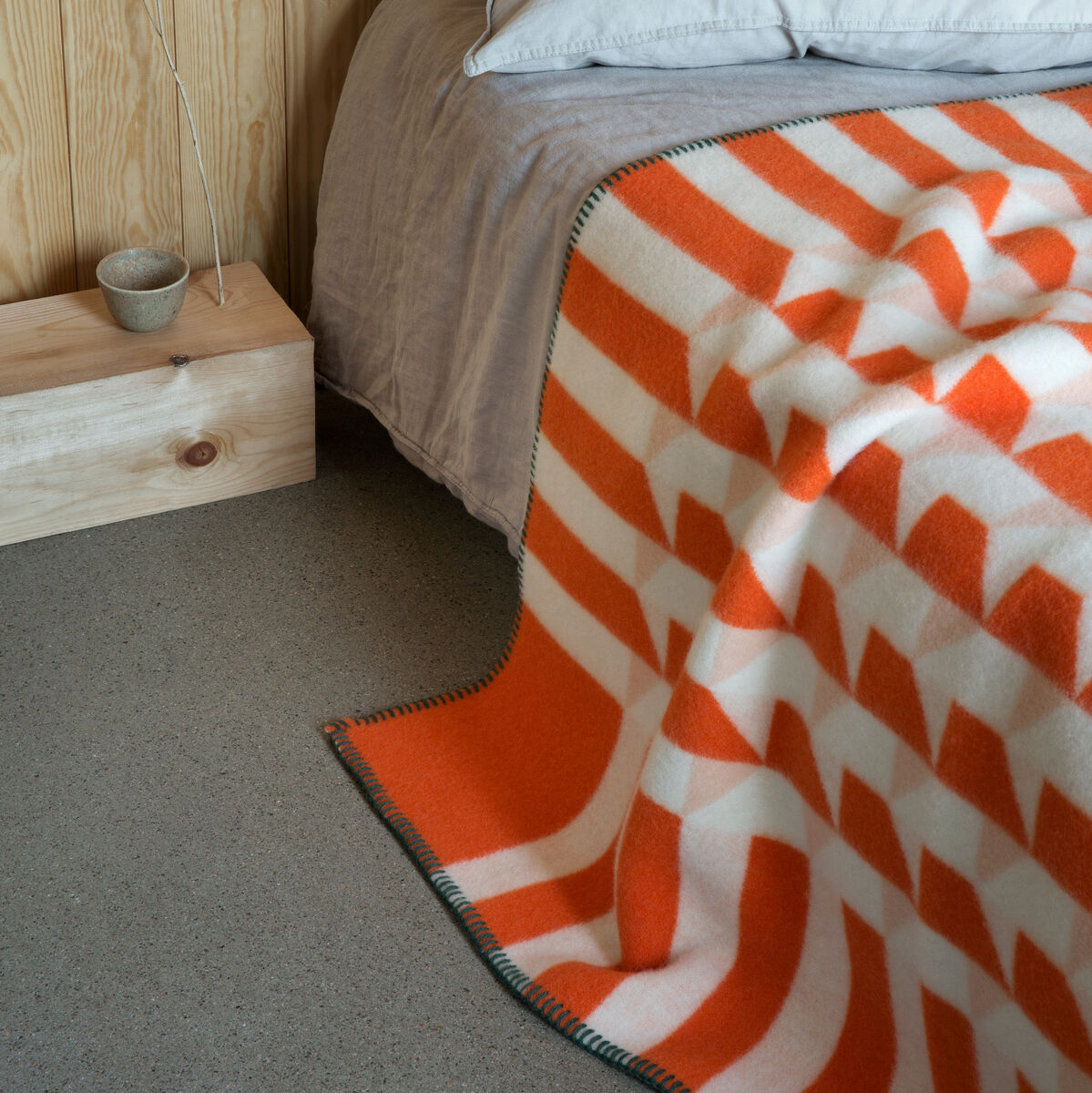 Eine Lammwolldecke »KVAM« in orange-weißem Muster liegt dekorativ auf einem Bett mit grauer Bettwäsche in einem gemütlichen Holz-Schlafzimmer.
